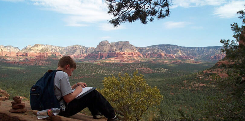 student writing in book overlooking red rocks of Sedona, Arizona.