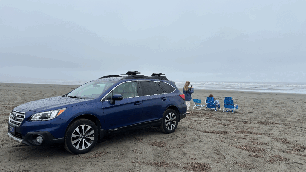 Car parked on the beach with beach chairs and people. 