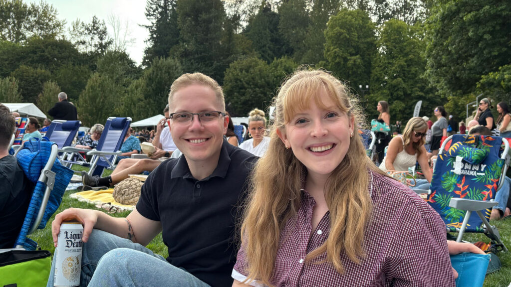 Emma and Spencer smiling and sitting on the grass at an outdoor concert.
