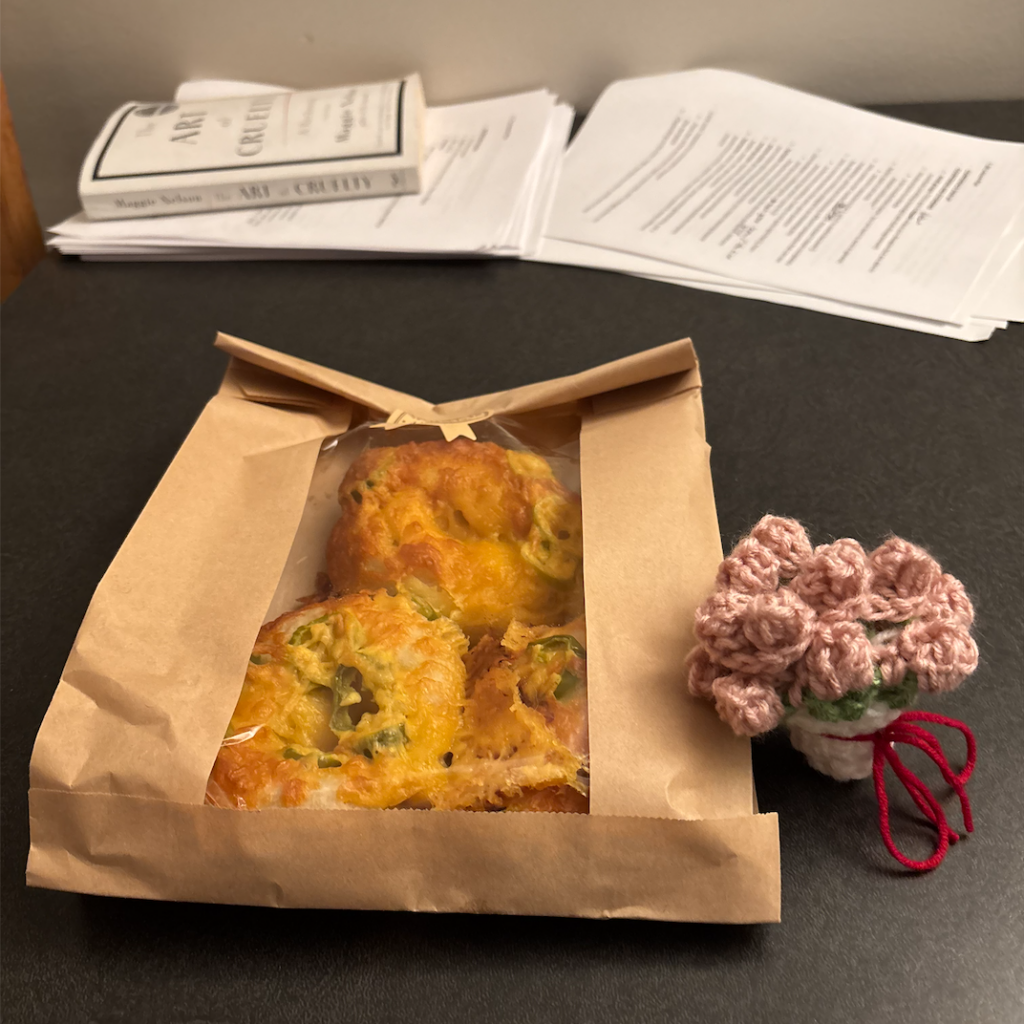 A bag of three bagels and a knitted coaster pulled up to look like a pot with flowers. 